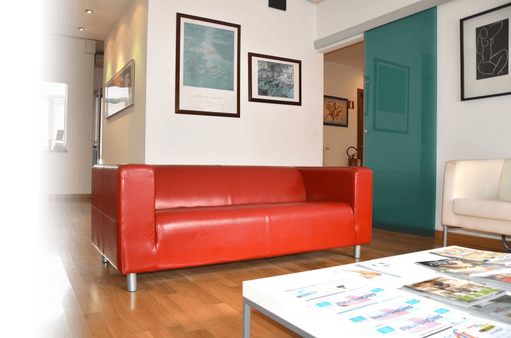 studio falduto odontoiatria specialistica Soggiorno con divano rosso e pareti decorate con quadri e mappe.